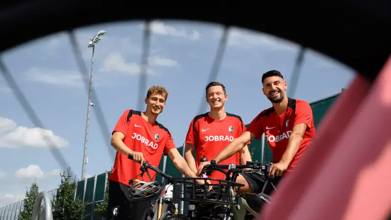3 SC Spieler stehen mit ihren Fahrrädern vor dem Stadion und grinsen in die Kamera 3 SC Spieler stehen mit ihren Fahrrädern vor dem Stadion und grinsen in die Kamera