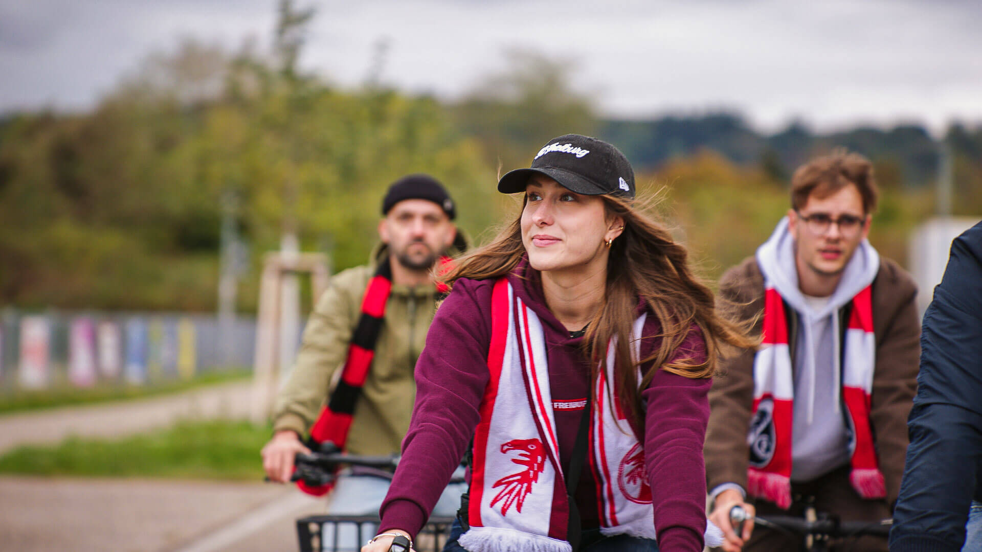 drei Fahrrad-Fans mit SC-Schals fahren mit dem Fahrrad zum Heimspiel des SC Freiburg